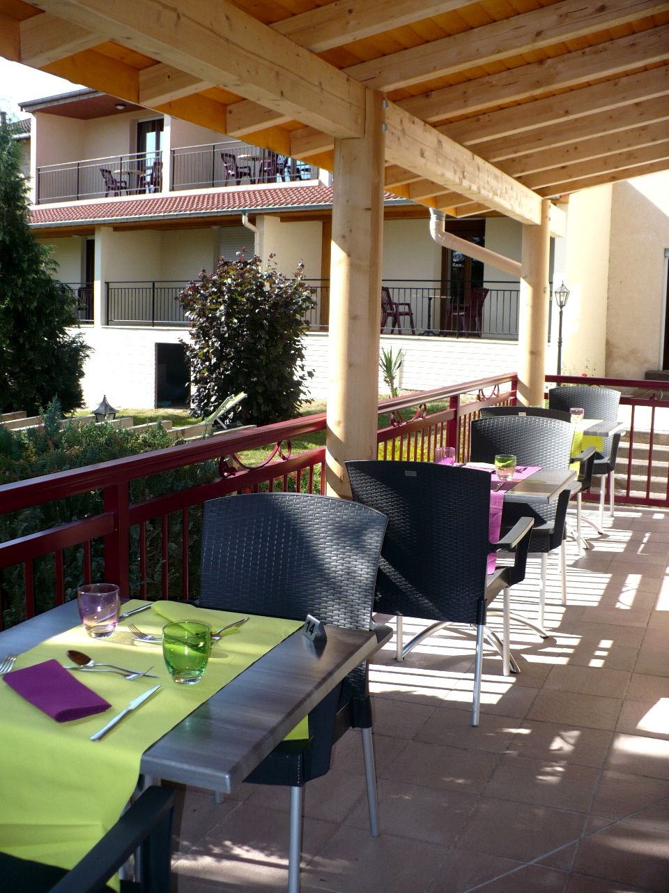 Un patio exterior con mesas y sillas, una pérgola de madera y vistas a un edificio con balcones.