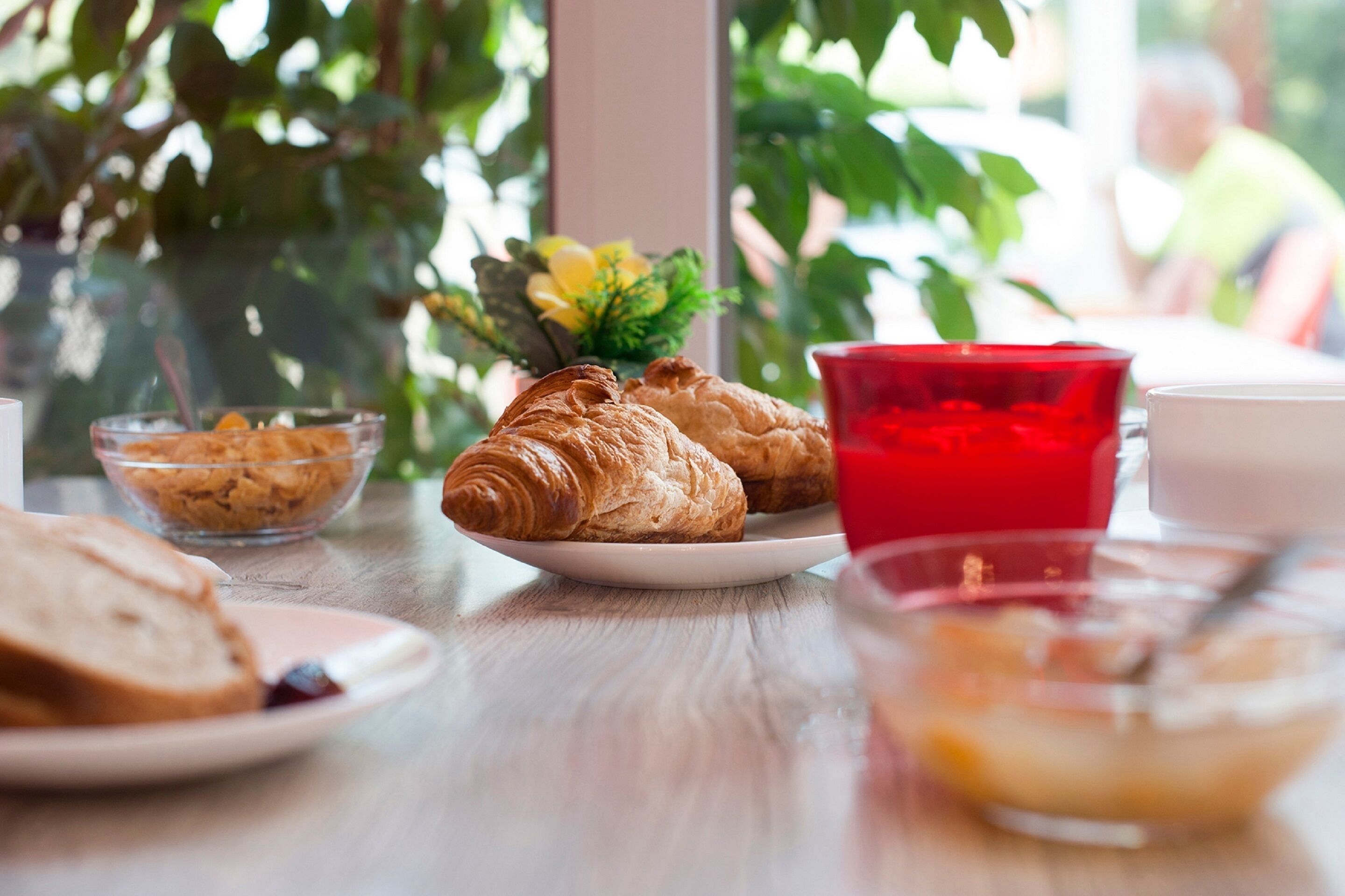 A breakfast table with croissants, a red glass, and a bowl of cereal.