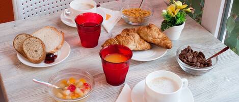 Una mesa con alimentos para el desayuno, incluyendo cruasanes, pan, cereales, fruta y bebidas.