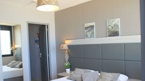Een moderne slaapkamer met een groot bed, een nachtkastje met een lamp, een kleine potplant en twee ingelijste foto's aan de muur.