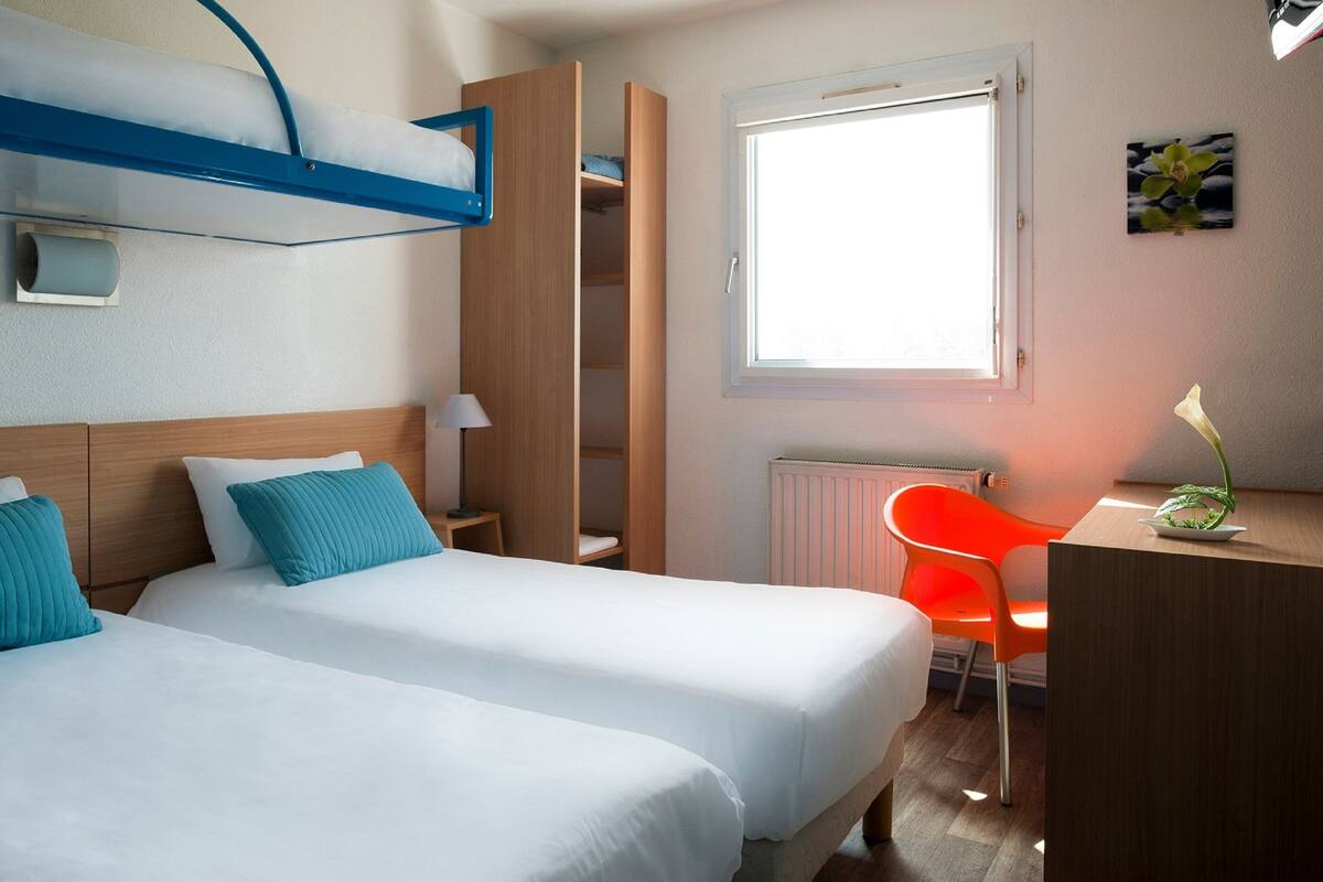 Ein Hotelzimmer mit zwei Betten, einem Schreibtisch, einem Stuhl, einem Heizkörper und einem Fenster mit Blick.