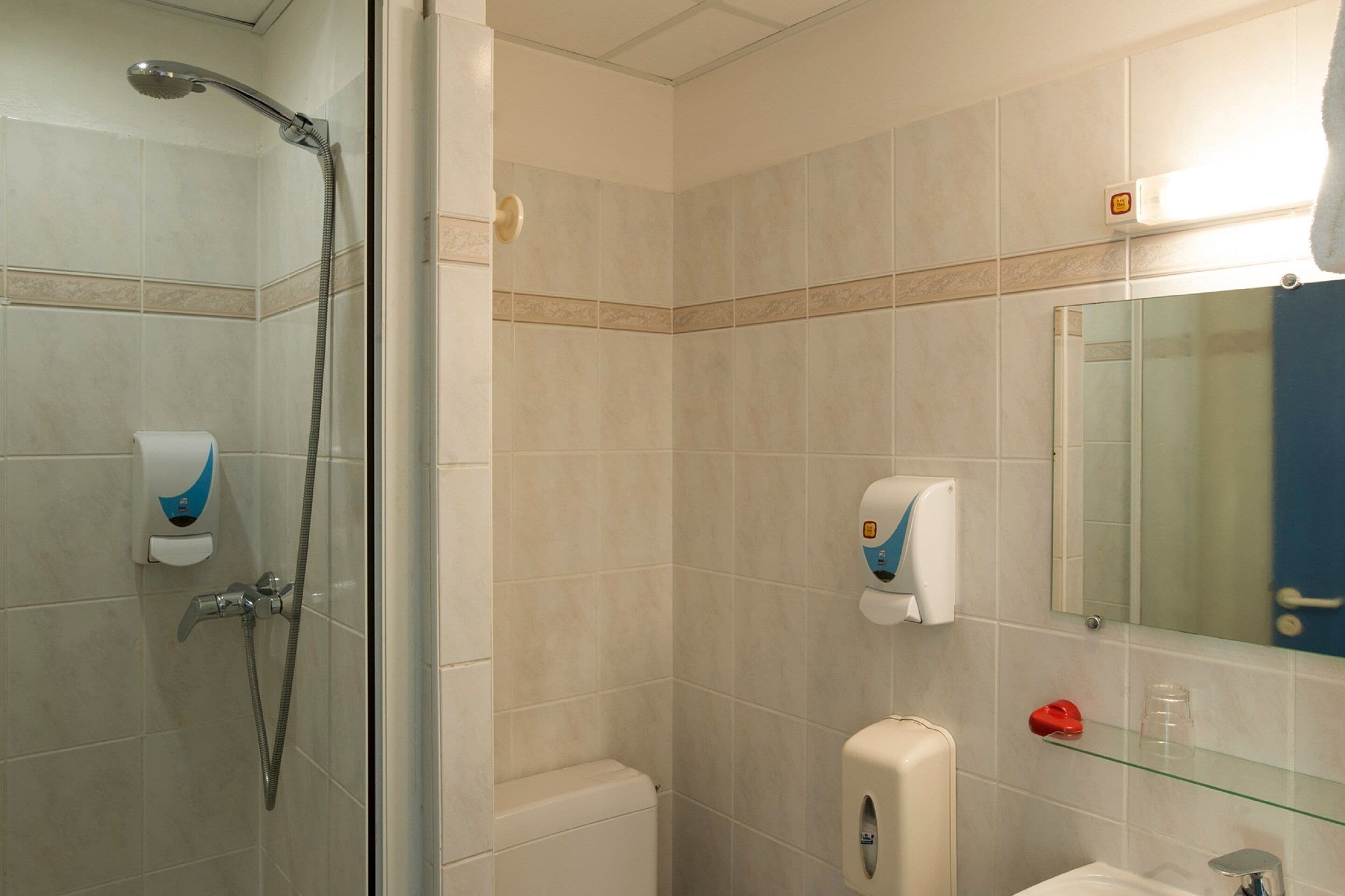Un baño con ducha, inodoro, lavabo y repisa de vidrio con artículos de aseo.