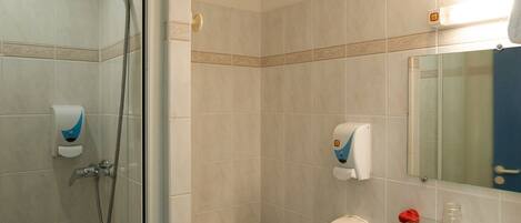 Un baño con ducha, inodoro, lavabo y repisa de vidrio con artículos de aseo.