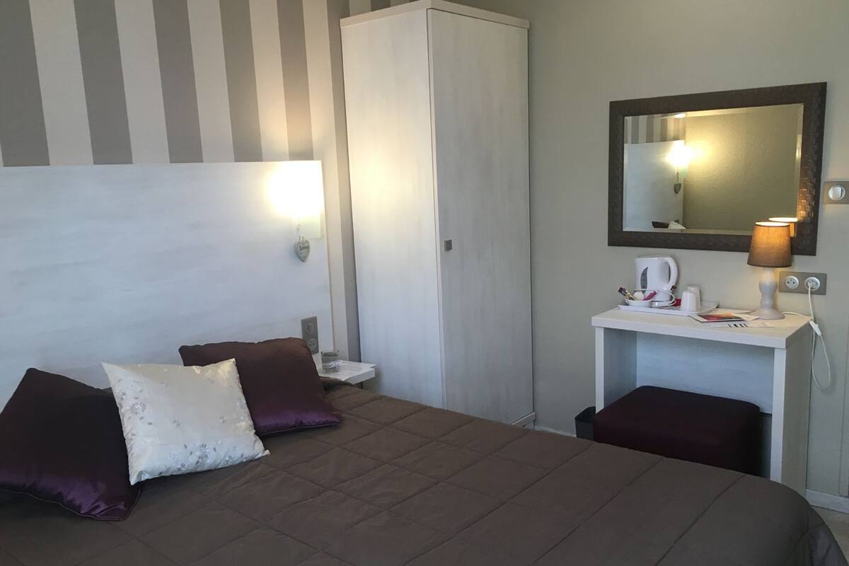 Ein Hotelzimmer mit Bett, zwei Kissen, einem Nachttisch mit Lampe, einem Kleiderschrank und einem Spiegel.