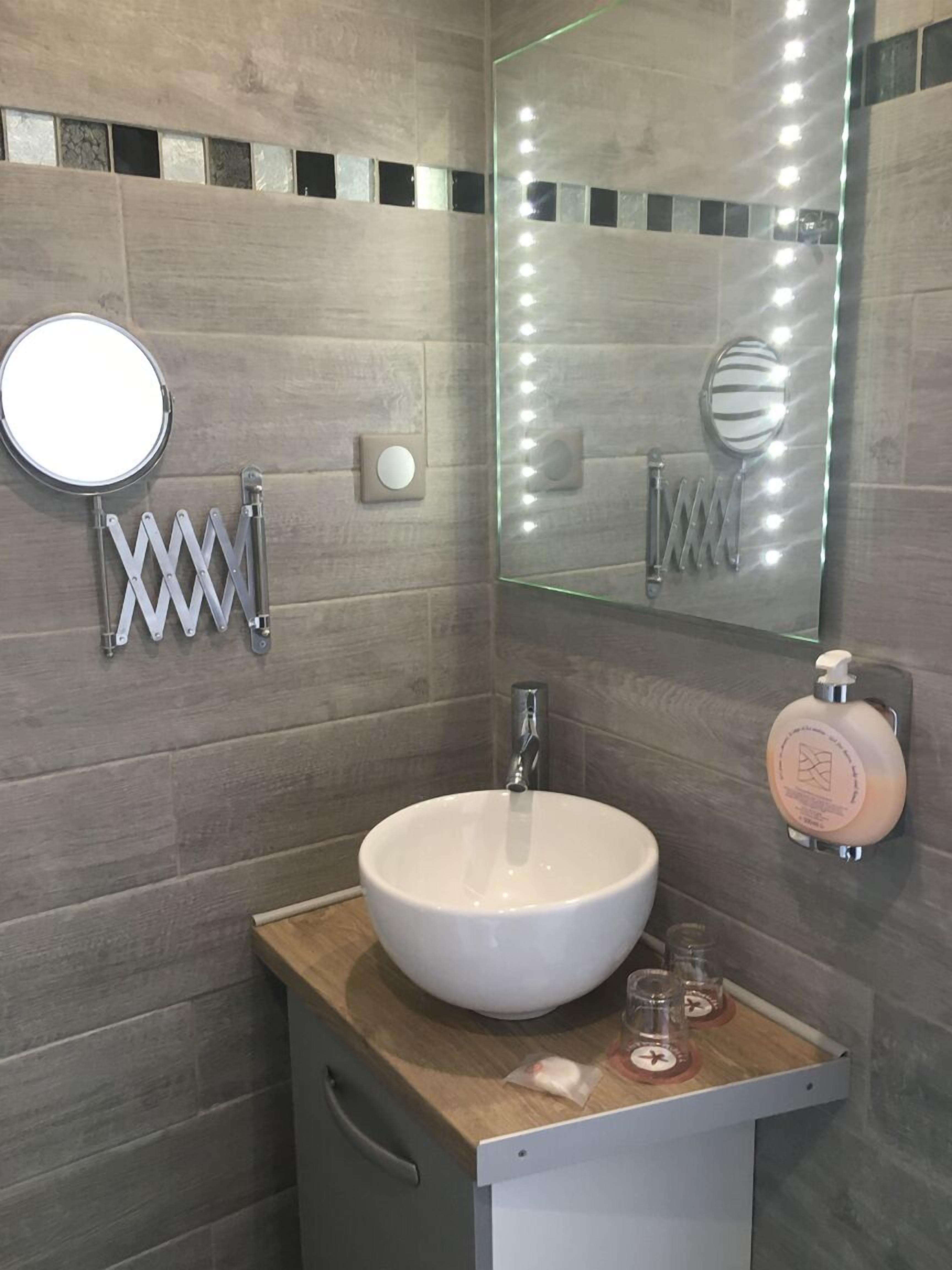 Un baño con un espejo redondo, un lavamanos blanco y un tocador con espejo.