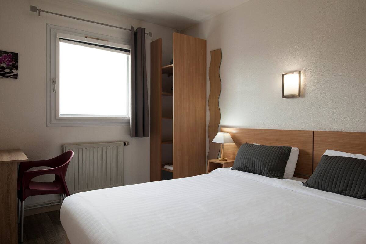 Ein Hotelzimmer mit Bett, Schreibtisch, Stuhl, Kleiderschrank und Fenster.