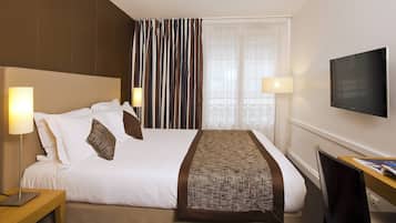 A hotel room with a bed, two bedside lamps, a TV, and a desk with a chair.