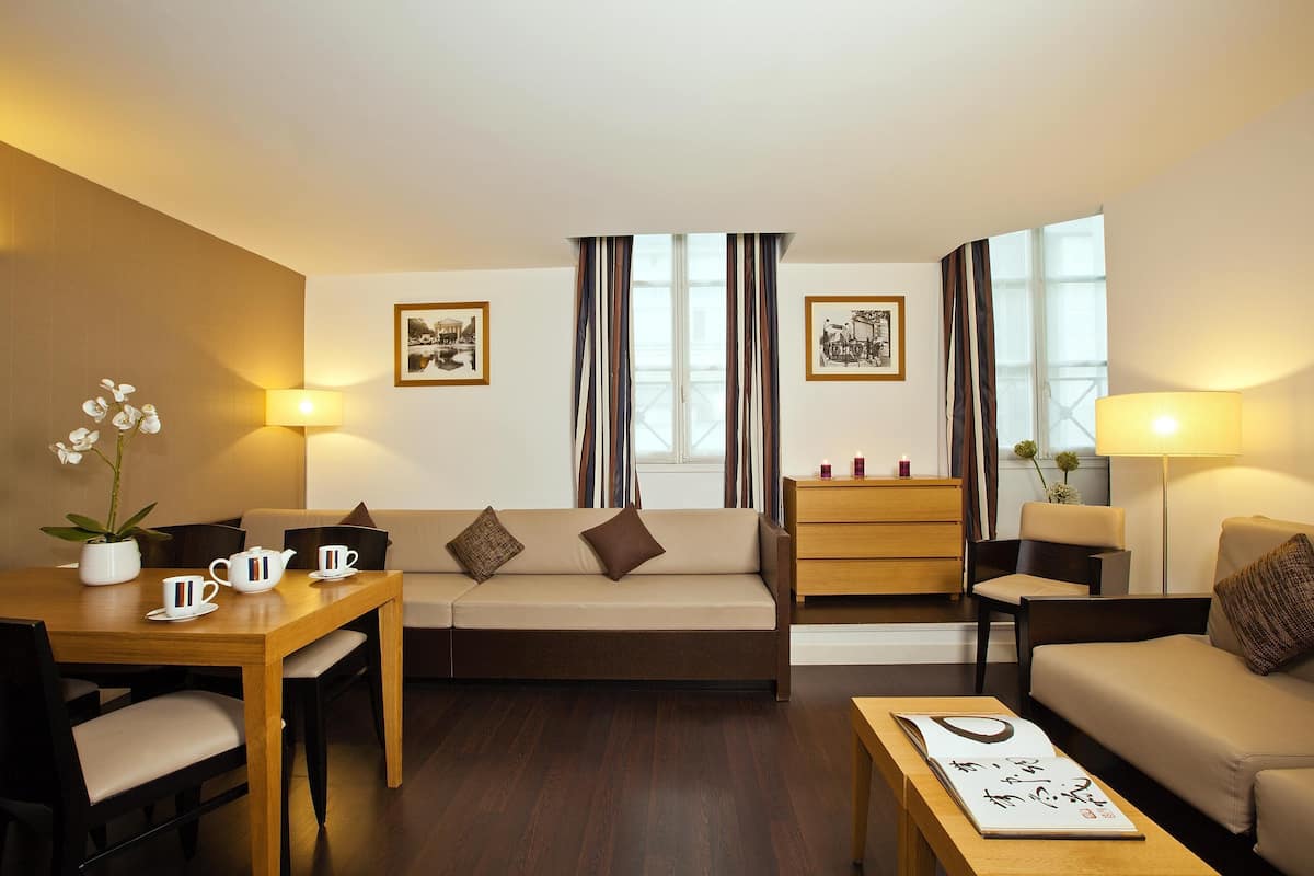 Un salon moderne comprenant un canapé, deux fauteuils, une table basse et une table à manger avec des chaises. On y trouve également deux lampes, une plante en pot et des tableaux encadrés accrochés aux murs.
