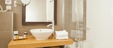 A modern bathroom with a large sink, a mirror, a shower, and a wooden cabinet with towels.