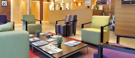 A lobby with a reception desk, several chairs, a coffee table with magazines, and a small plant.
