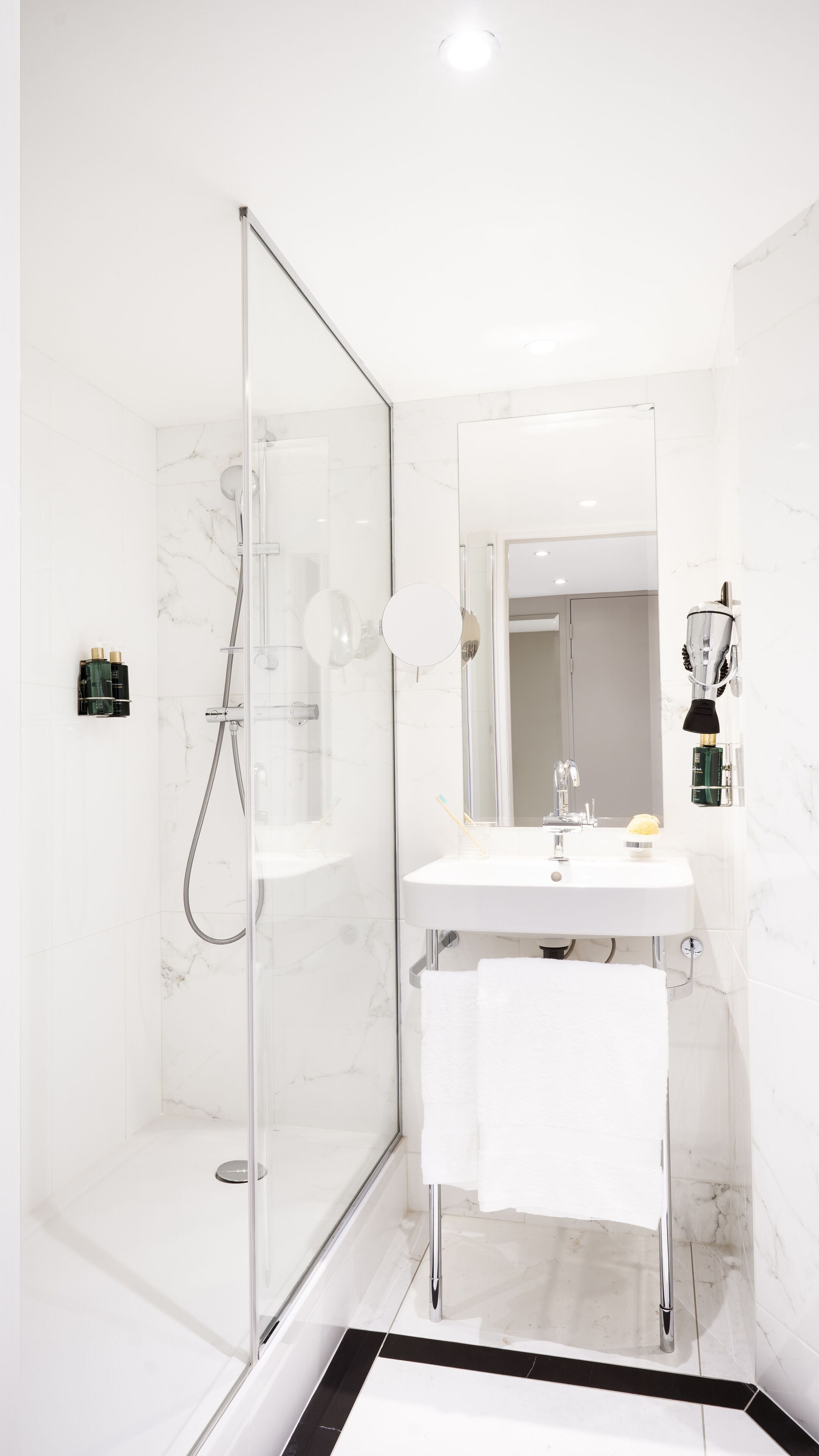 Un baño moderno con ducha envuelta en vidrio, lavamanos blanco y un espejo grande.