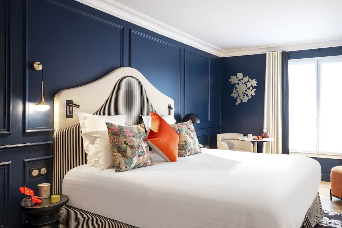 Une chambre d’hôtel moderne avec un grand lit, une petite table avec une théière et un téléviseur.