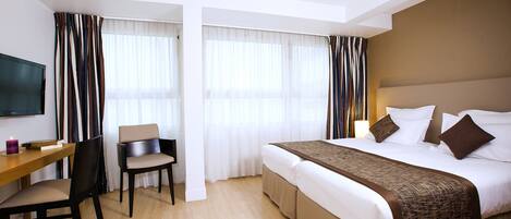 A hotel room with a bed, a desk, a chair, and a television.