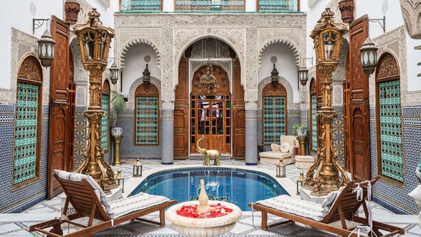 Une cour somptueuse avec une piscine, des meubles en bois et des motifs complexes en mosaïque.