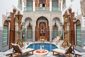 An ornate courtyard with a pool, wooden furniture, and intricate tile work.