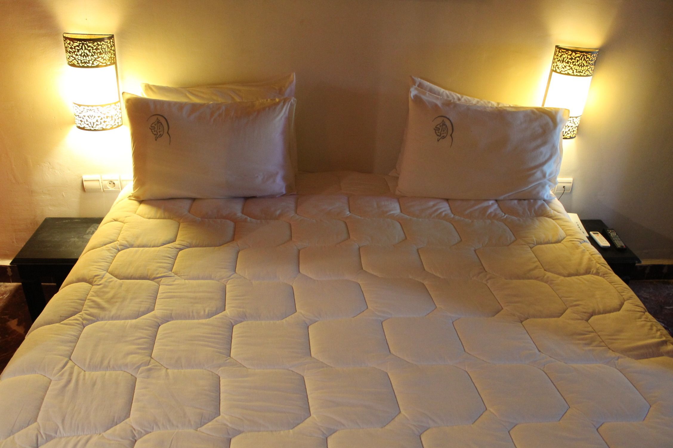A bed with a quilted cover and two pillows, flanked by nightstands with lamps.