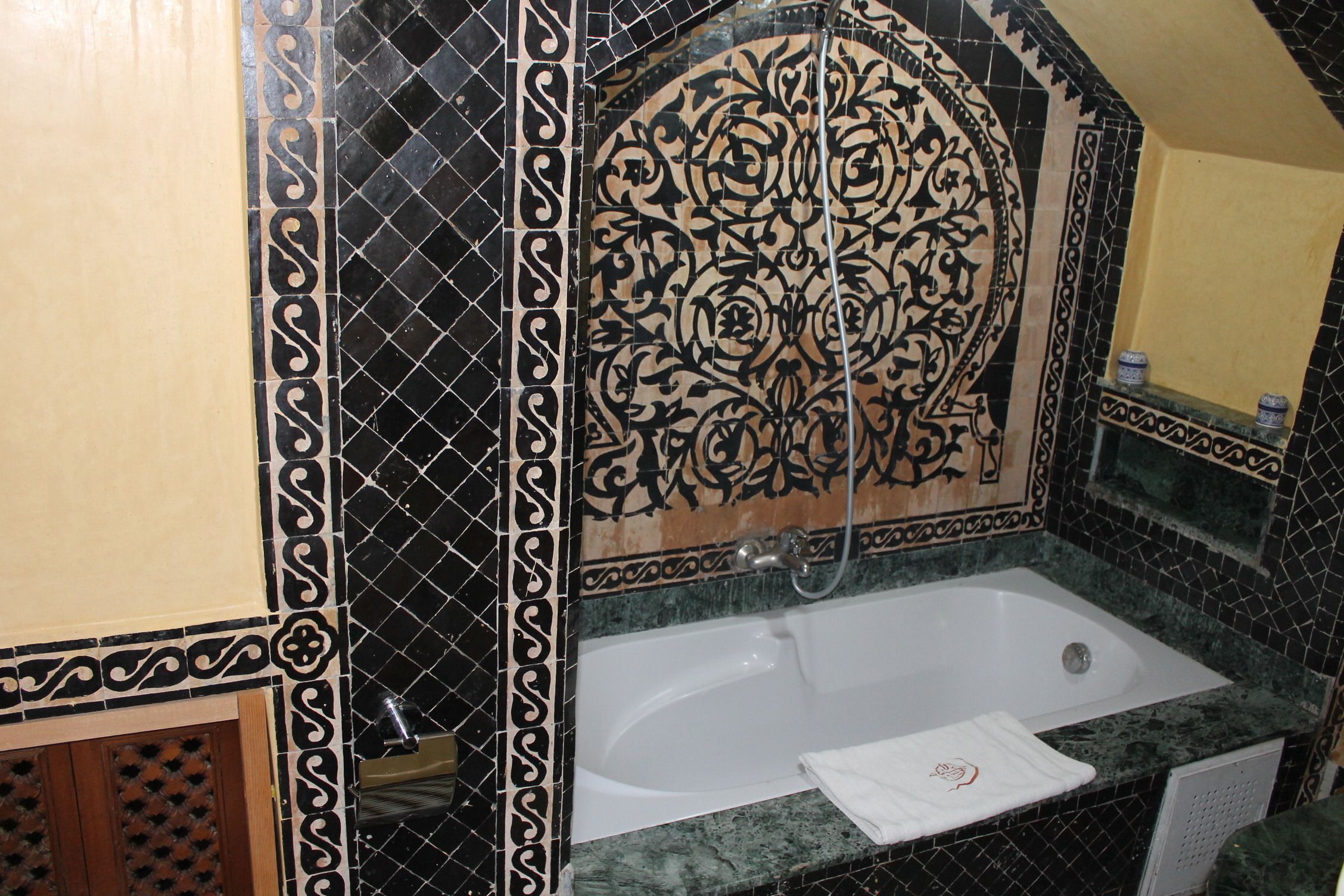 A bathroom with a bathtub, a shower, and a sink. The walls are decorated with black and white patterned tiles.