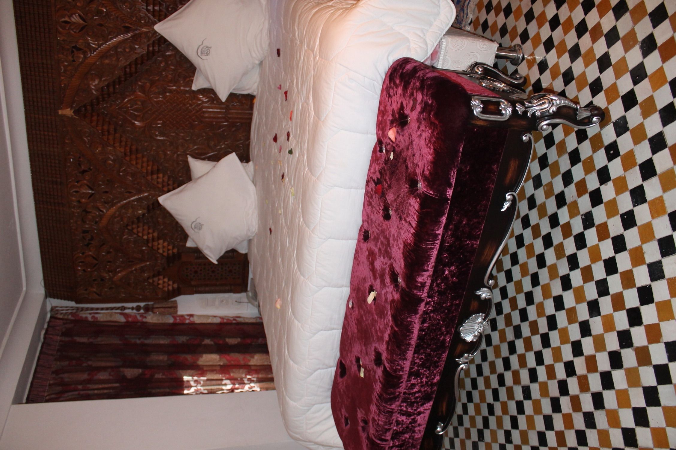 A bed with a white quilt and pillows, a red velvet suitcase, and a checkered wall.