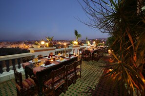 Enjoy a meal with a view at this outdoor dining area, featuring a beautifully set table and a scenic cityscape backdrop.