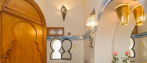A bathroom with a wooden door, a sink with a yellow and blue tiled backsplash, and a mirror with a decorative frame.