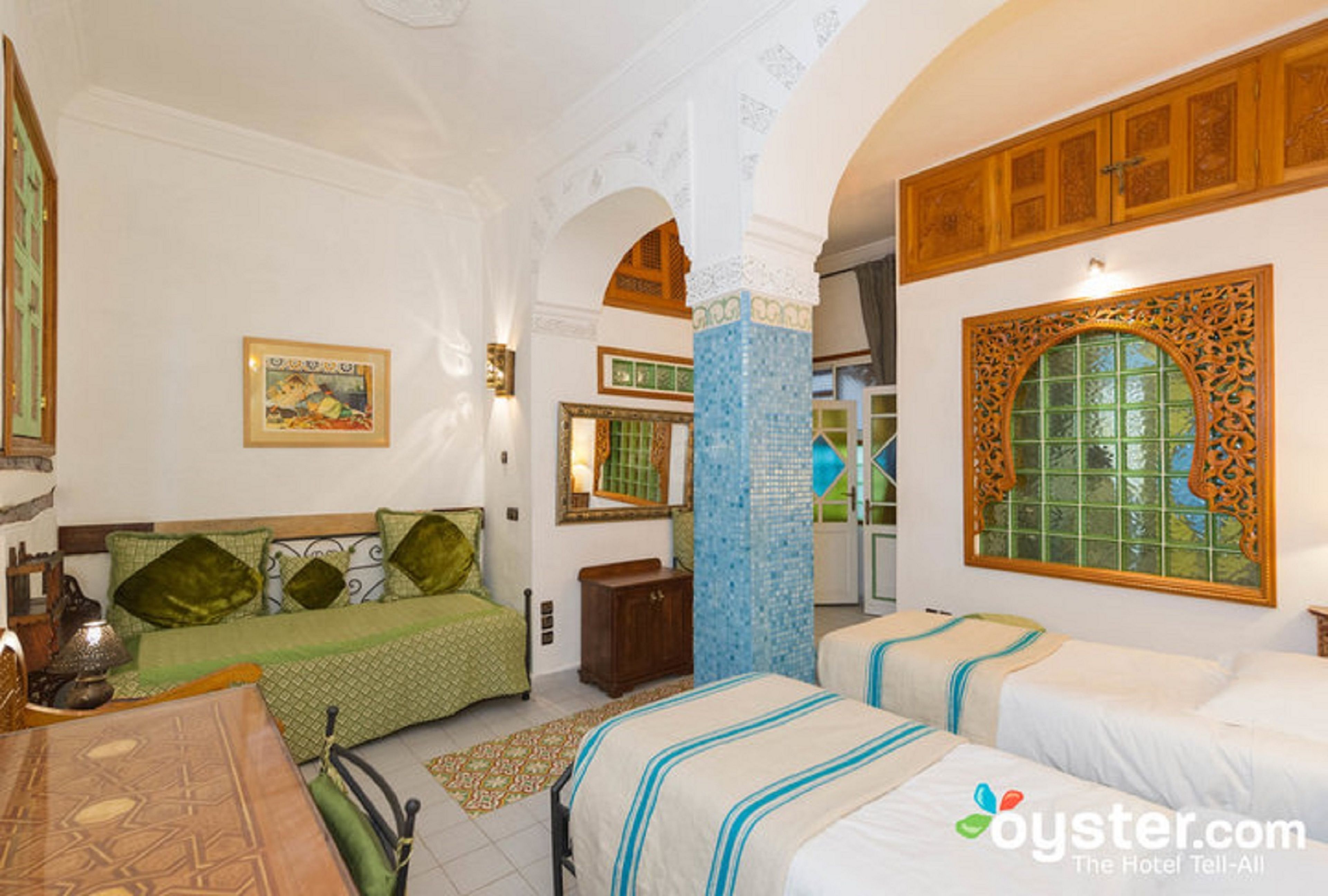 Una habitación de hotel con cama, sofá, mesa de comedor y un ventanal decorativo.