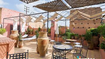 Un patio al aire libre con mesas y sillas, rodeado de plantas en macetas y grandes jarrones.