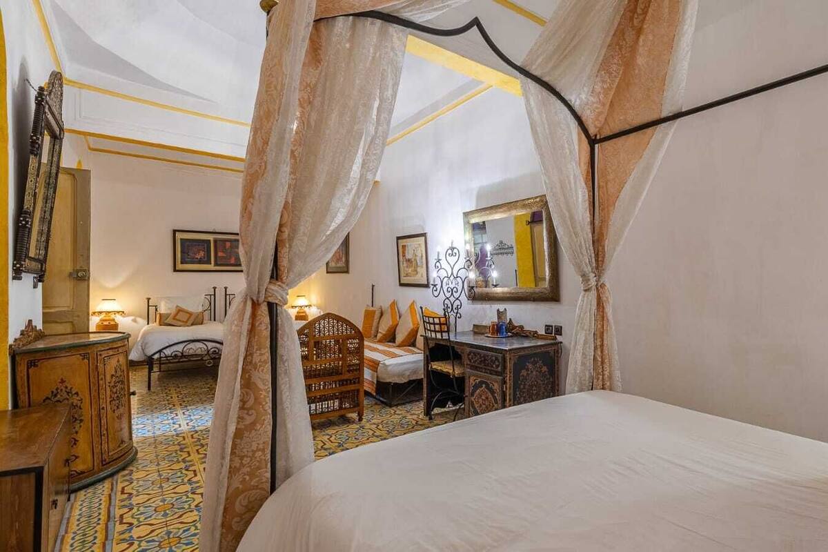 Un dormitorio con cama a dosel, un escritorio de madera, una silla, un aparador y un espejo.