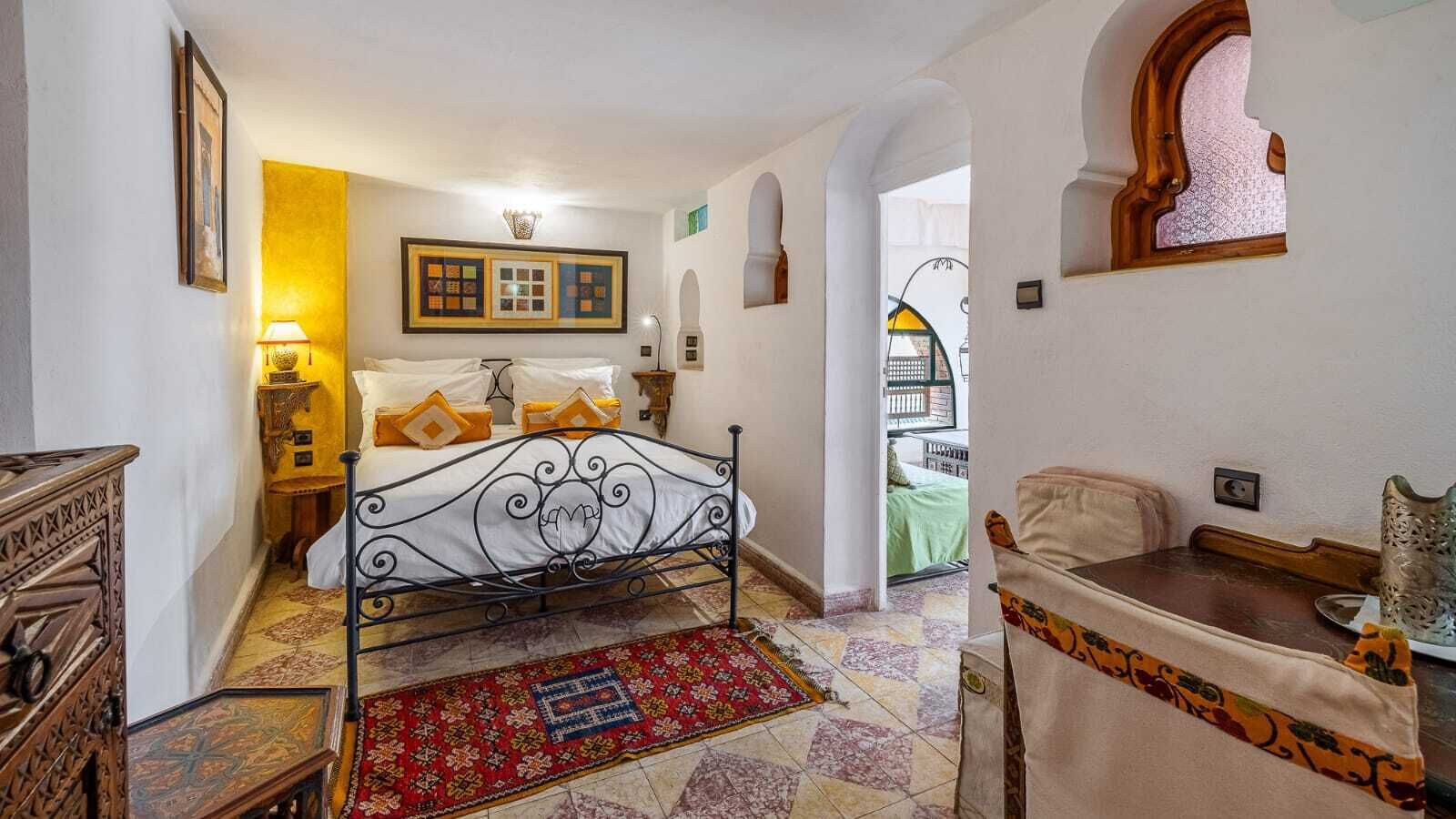Un dormitorio con cama, mesita de noche, lámpara, silla y mesa con un florero.