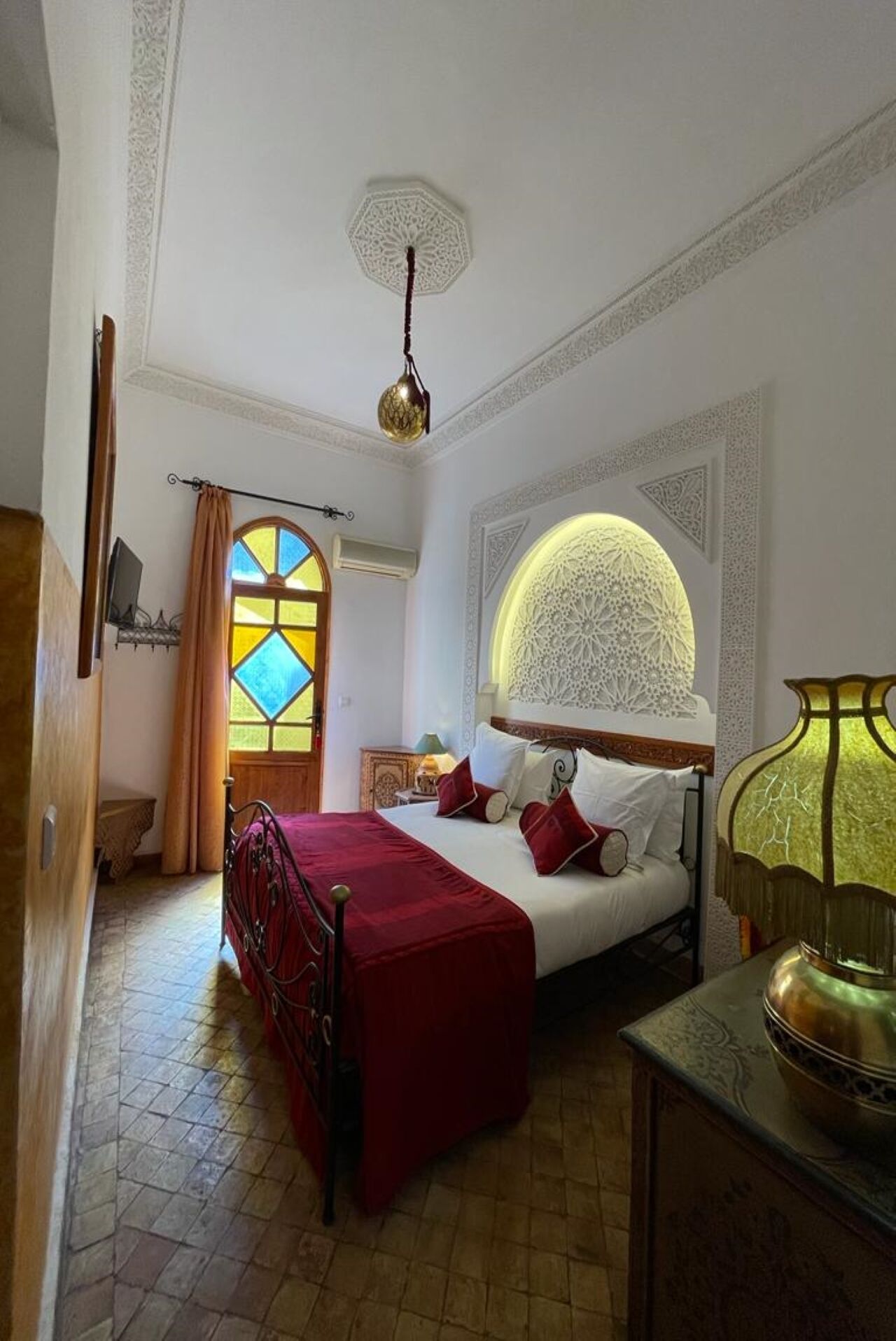 Un dormitorio con una cama grande, una mesita de noche, una lámpara y una ventana con vidrieras.