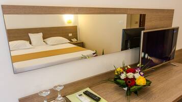 A hotel room with a bed, bedside table, mirror, TV, flowers, and a remote control.