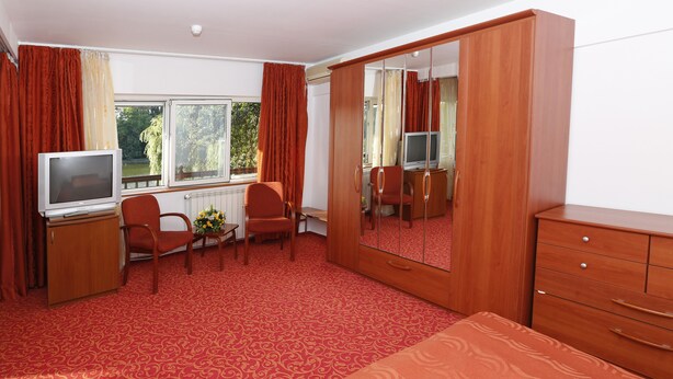 A hotel room with a large wardrobe, a bed, a desk with a television, and a window with curtains. - Hotel Herastrau (Bucharest)