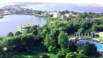 A resort with a large swimming pool surrounded by lush greenery and a view of a lake.