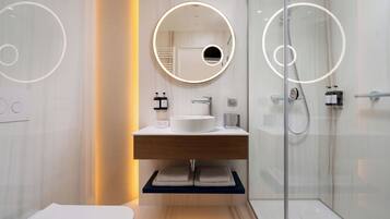 Un baño moderno con un espejo redondo, un lavabo y una cabina de ducha de vidrio.