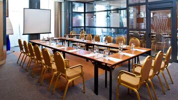A conference room with a long table, multiple chairs, a projector screen, and a glass partition.