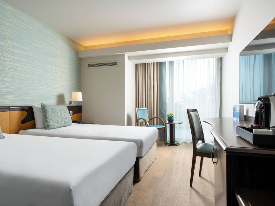 Habitación de hotel con dos camas, un escritorio con cafetera, una silla y un televisor.