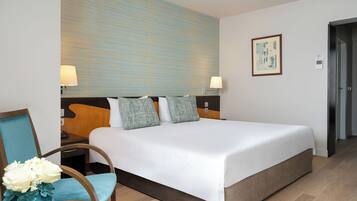 A hotel room with a large bed, two bedside tables with lamps, a chair with a vase of flowers, and a painting on the wall.