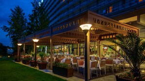 An outdoor dining area with tables and chairs, surrounded by planters and a covered walkway.