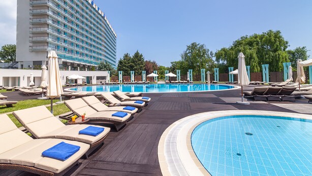 A hotel pool area with lounge chairs and umbrellas, a large pool, and a building with balconies.