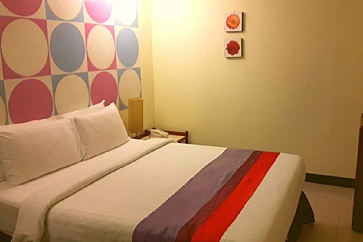 Hotellihuone, jossa on sänky, yöpöytä, lamppu ja televisio.