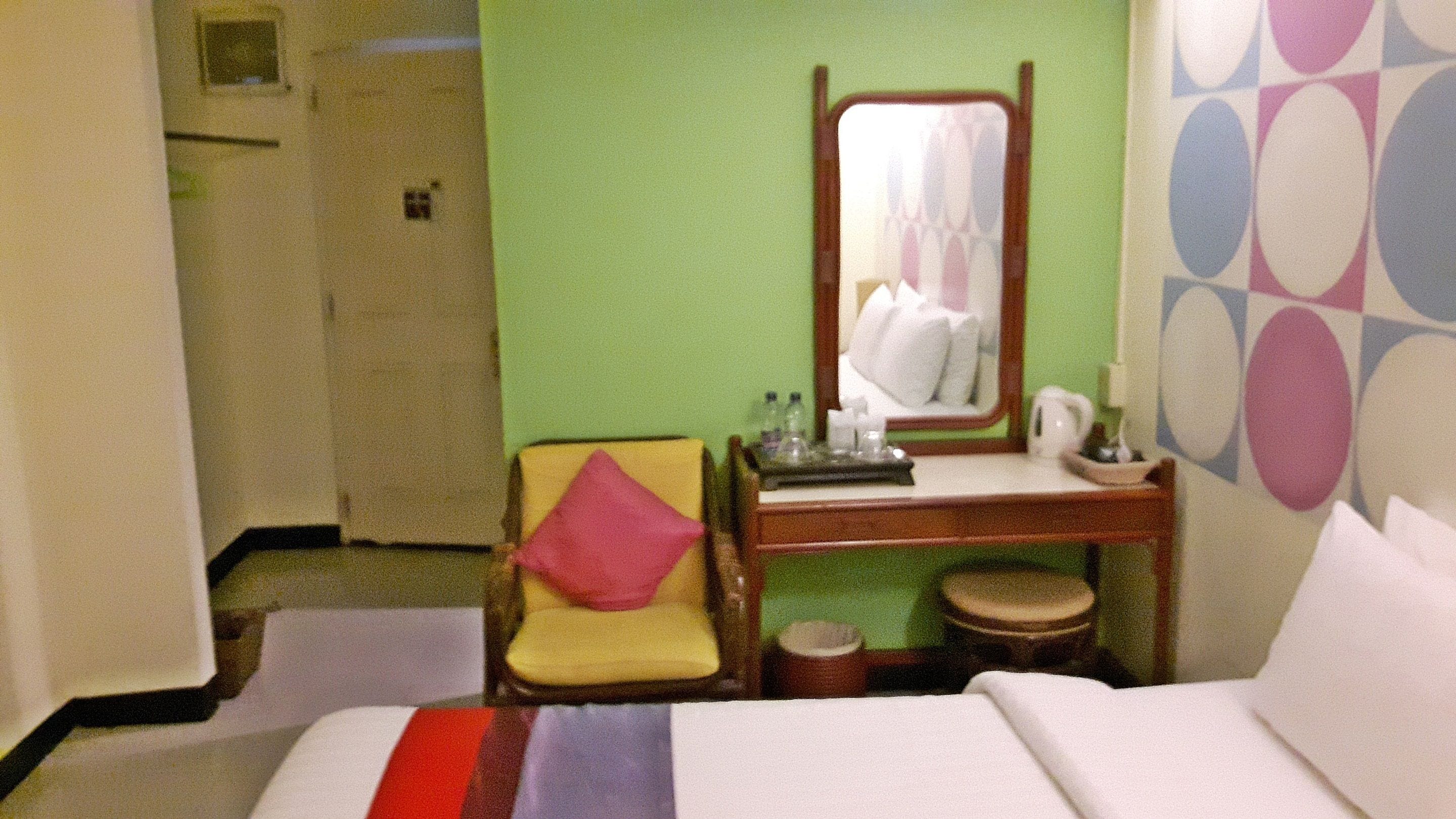 Habitación de hotel con cama, un escritorio pequeño, una silla, un espejo y una pared con un diseño geométrico.