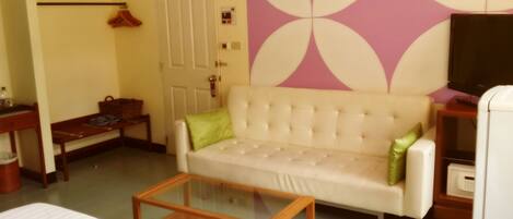Una sala de estar con un sofá, una mesa de centro de vidrio, un televisor y una puerta.
