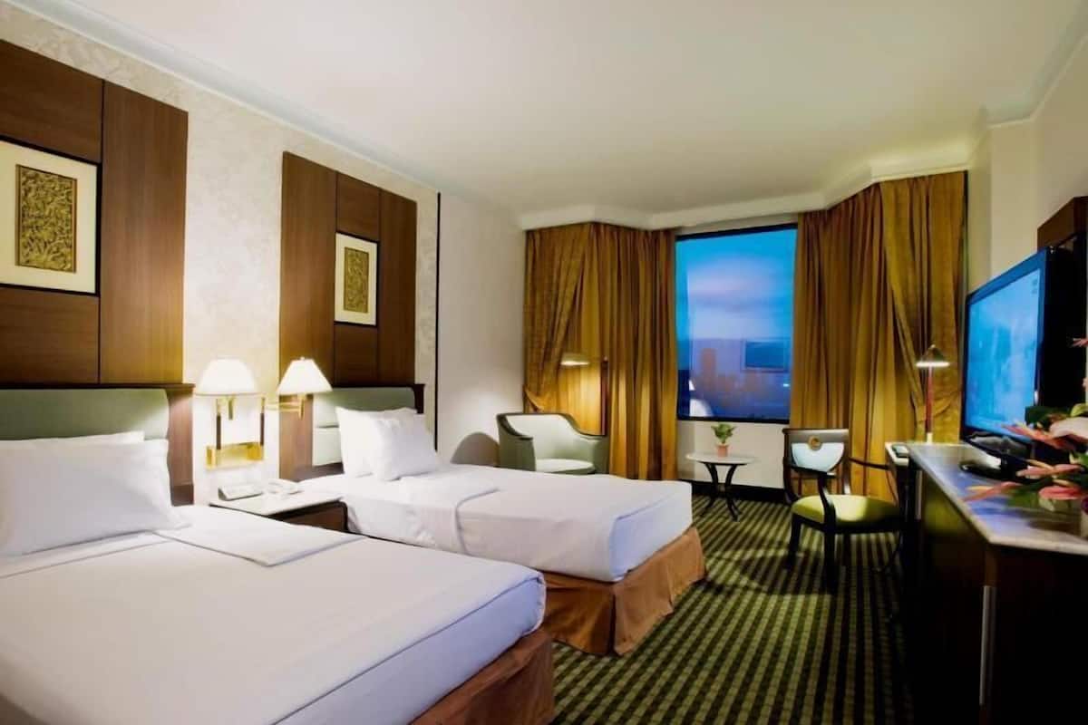A hotel room with two beds, a desk, a chair, a TV, and a window with curtains.