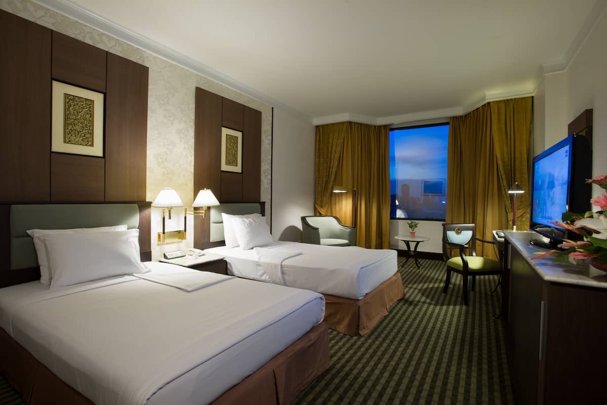 A hotel room with two beds, a desk, a chair, a TV, and a window with curtains.