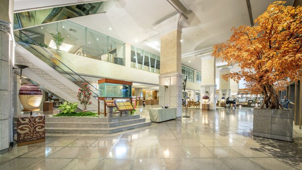 Un vestíbulo espacioso con piso pulido, una escalera y un árbol artificial grande.
