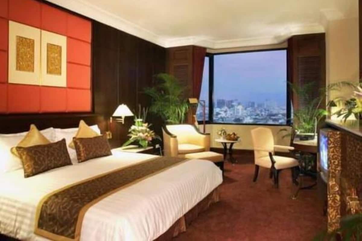 A hotel room with a large bed, a sitting area with a table and chairs, and a view of a cityscape through a large window.