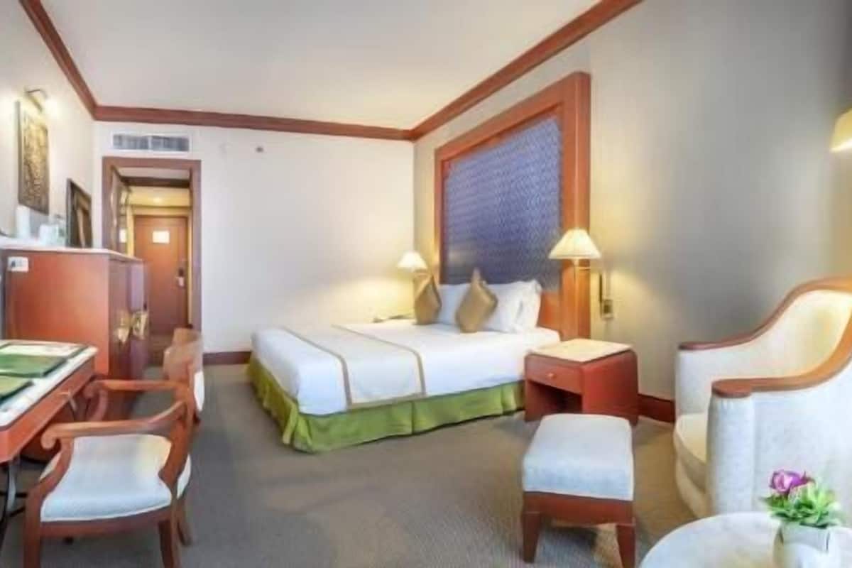 A hotel room with a bed, a desk, a chair, a nightstand, and a lamp.