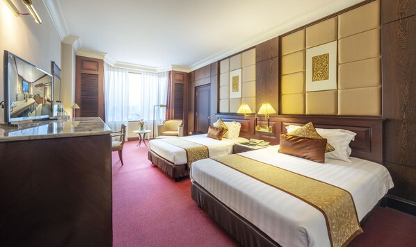 A hotel room with two beds, a desk, a chair, a small table with a vase, and a large mirror.
