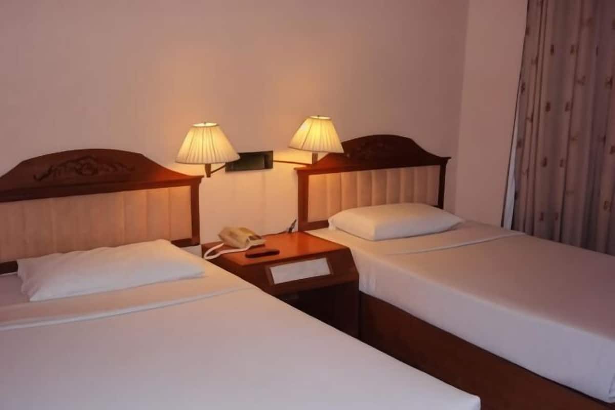 A hotel room with two beds, bedside lamps, a nightstand with a phone, and a curtain.