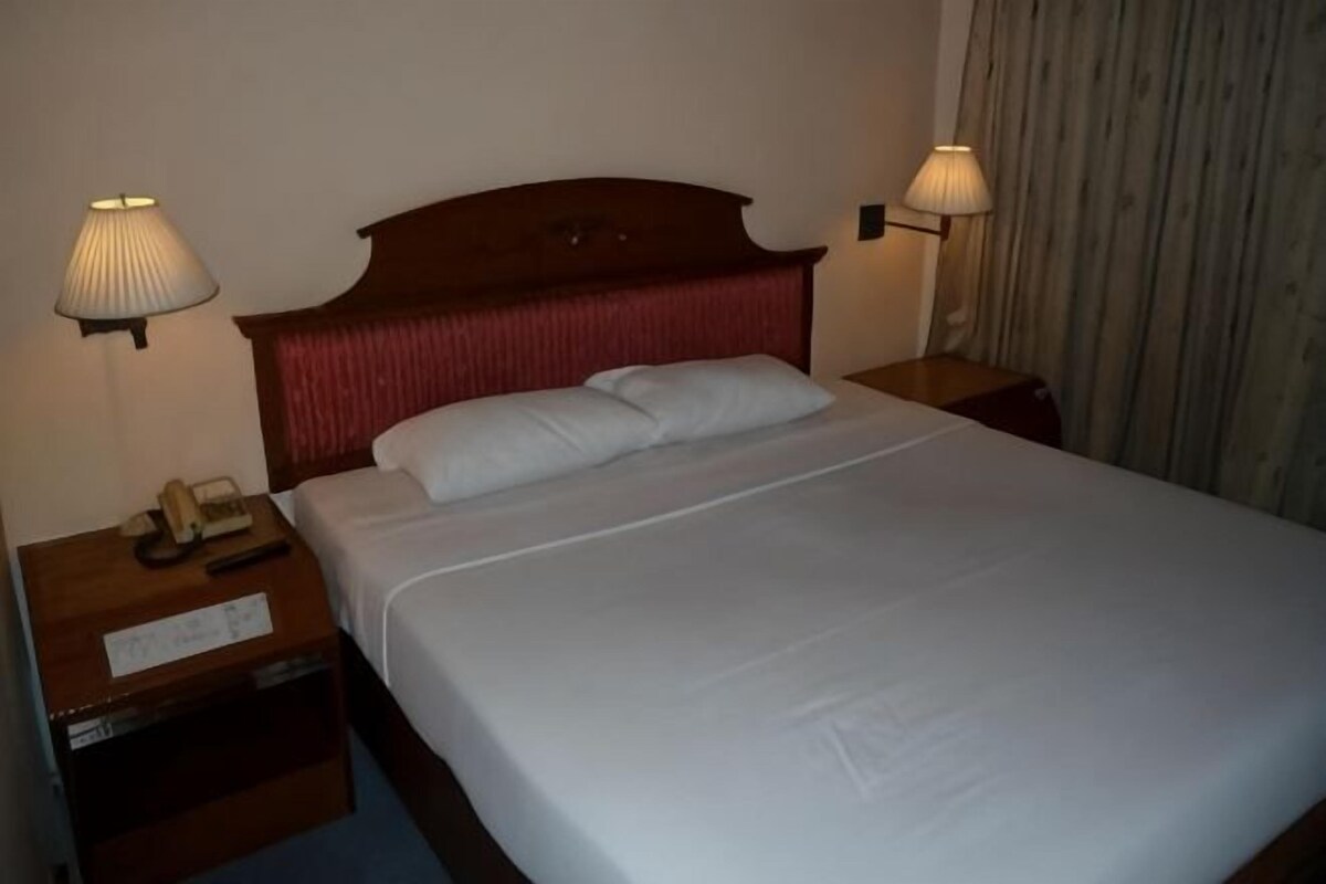 A hotel room with a bed, two bedside lamps, a nightstand with a telephone, and a curtain.