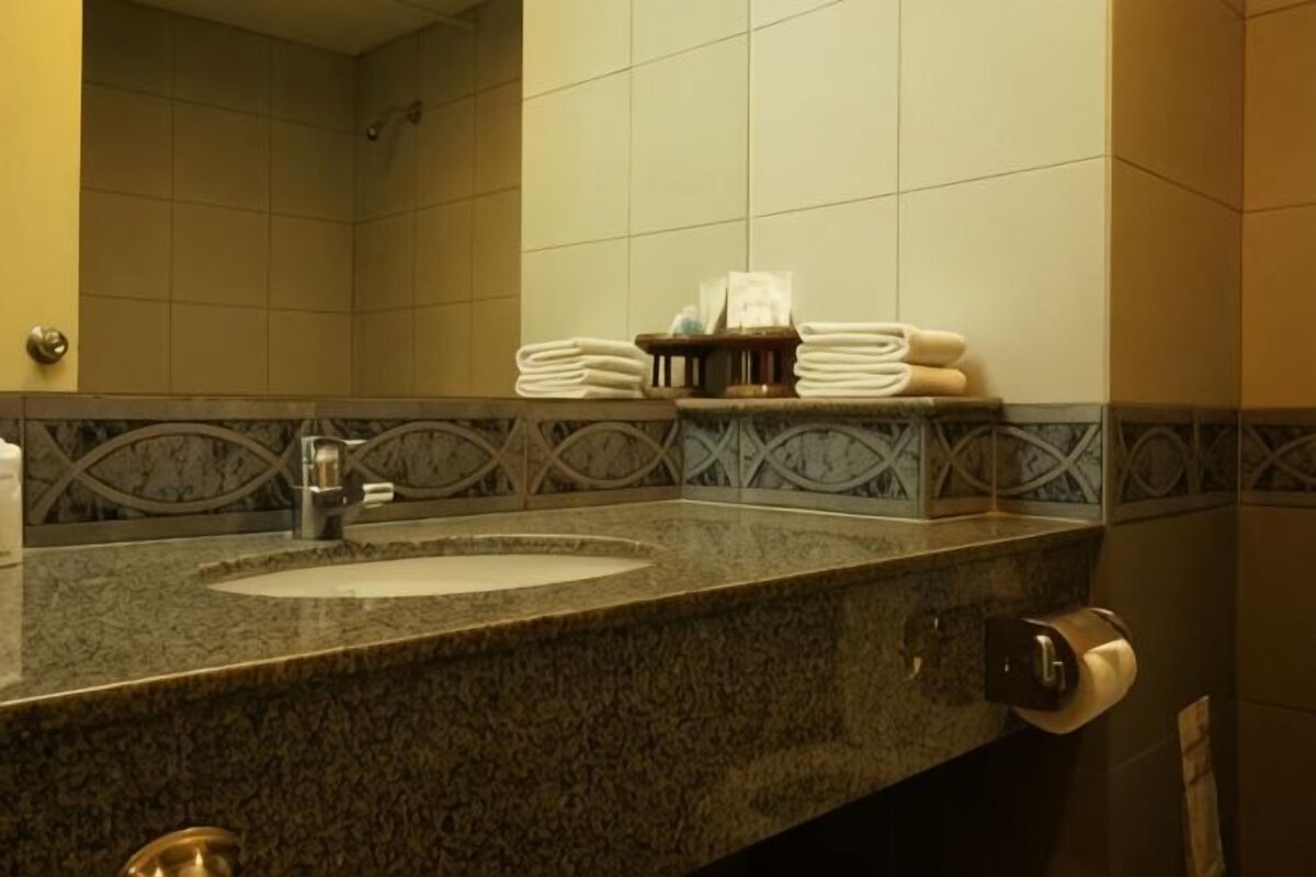 A bathroom with a granite sink, a towel rack with folded towels, and a mirror.